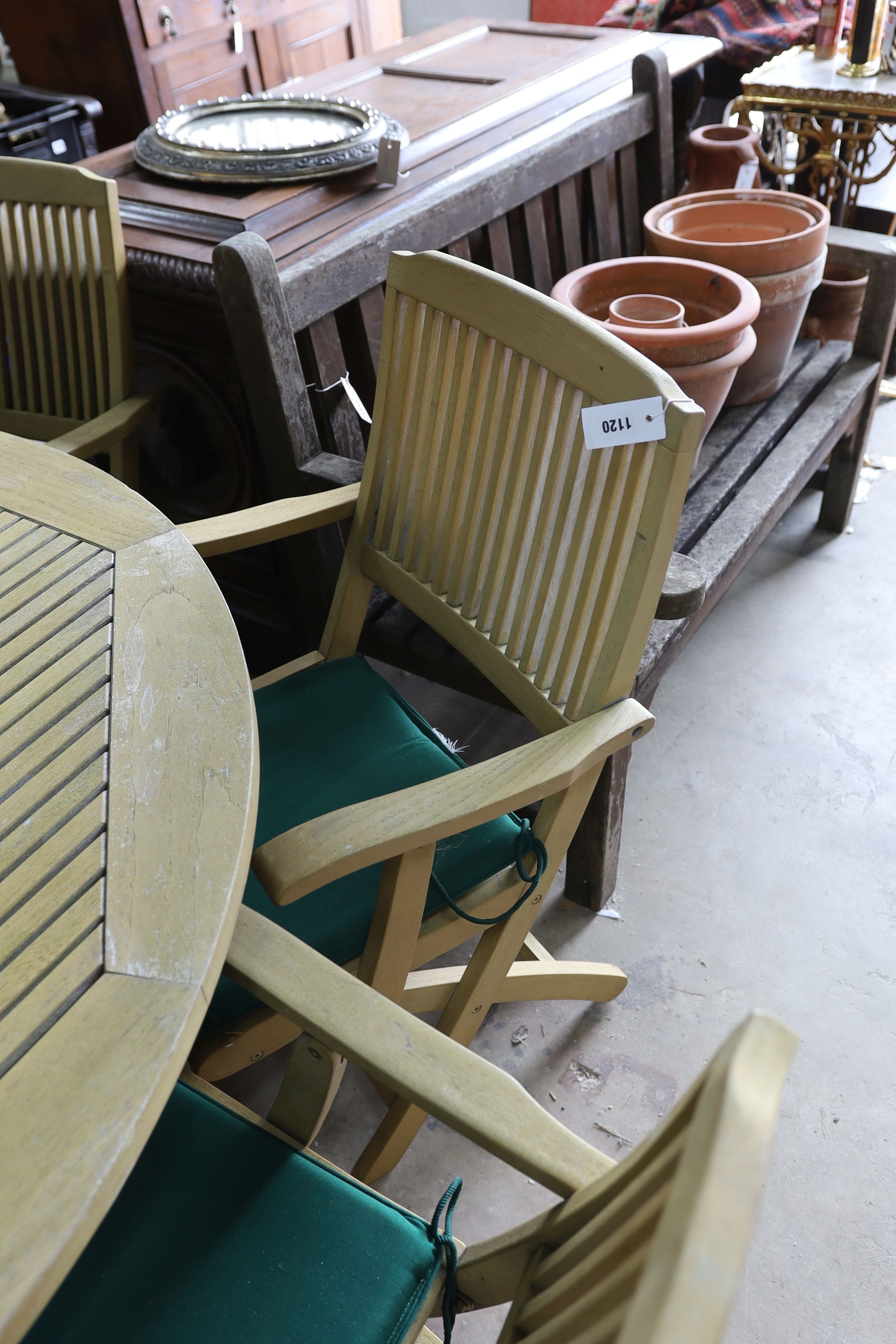 A teak garden set comprising circular table 148 cms diameter height 75 cms with 'Lazy Susan', parasol and waterproof cover and metal base, six folding elbow chairs and seat cushions.